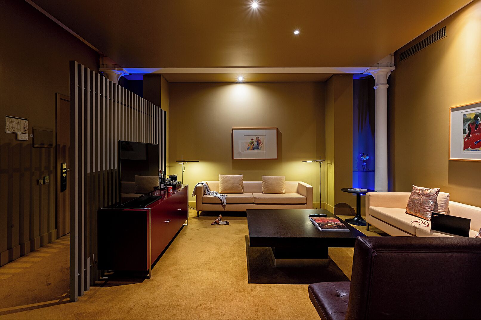 Una sala de estar moderna con un sofá, una mesita de centro y un televisor. Se observa un mueble de almacenamiento rojo y una lámpara de pie.