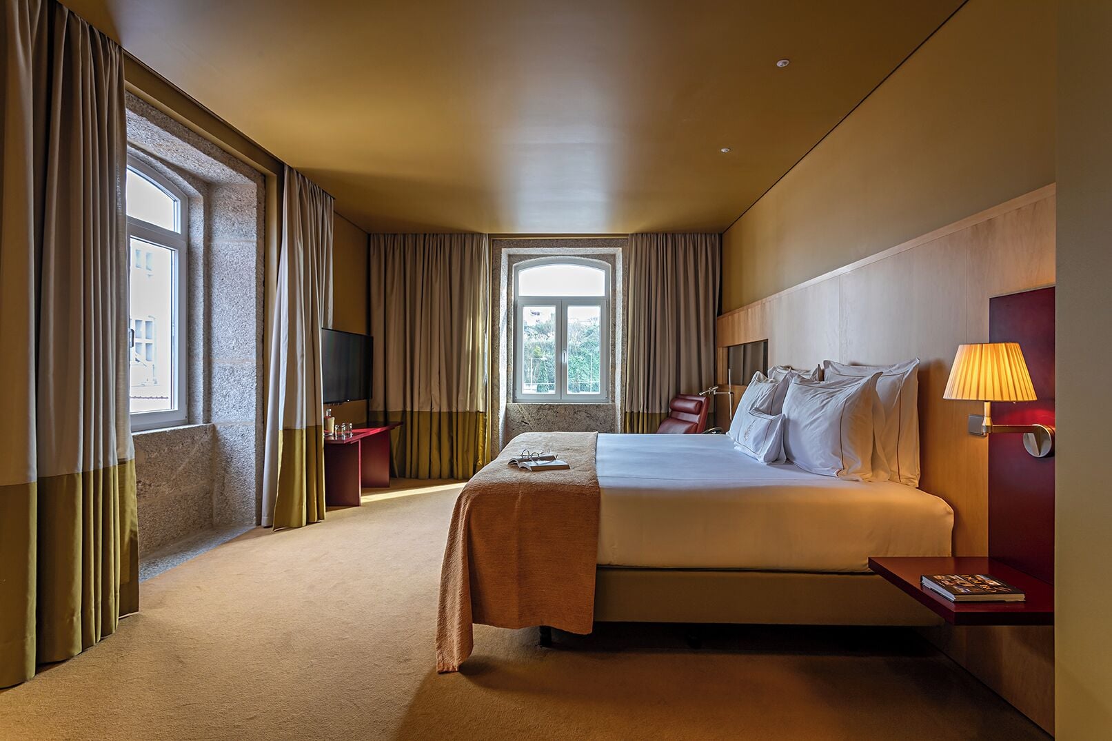 A hotel room with a large bed, a desk, a chair, a TV, and a window with curtains.