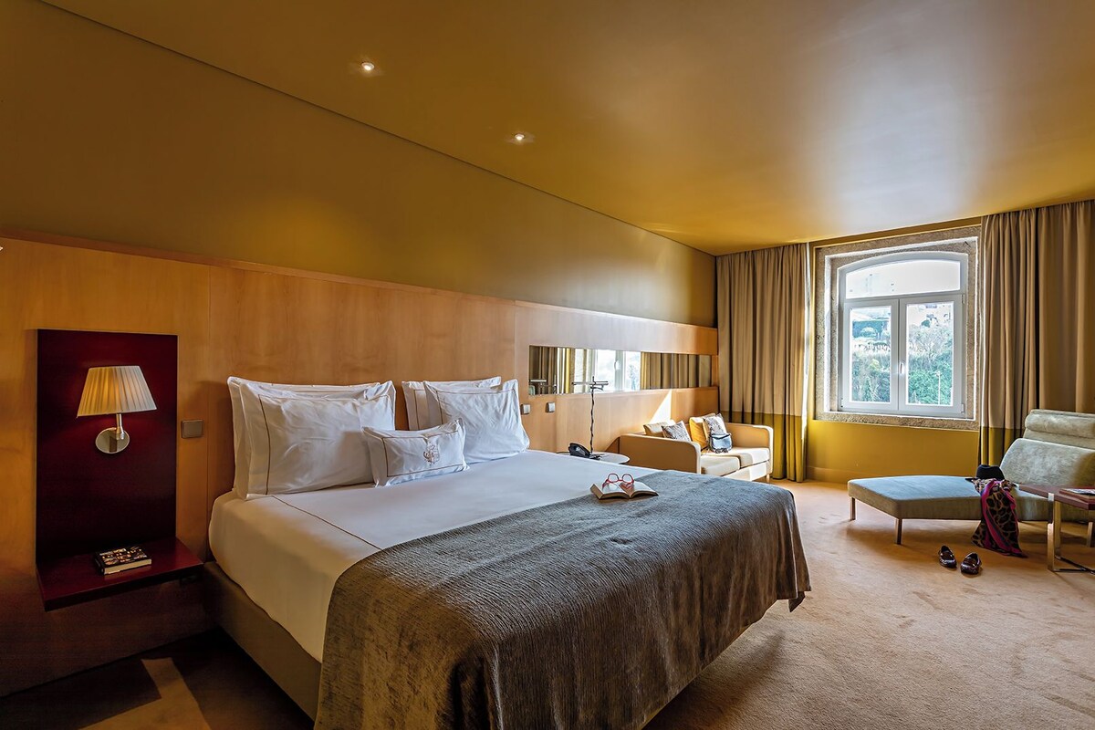 Habitación de hotel con una cama grande, mesitas de noche, un escritorio, una silla y una ventana con cortinas.