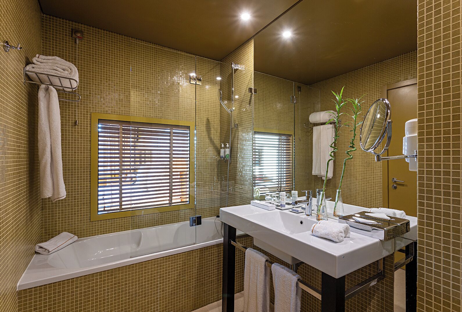 A bathroom with a bathtub, a large mirror, and a window with blinds.