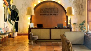 Una recepción con un cartel que dice "BANZIL BY EARANDA BOUTIQUE", una computadora portátil, dos lámparas, una silla pequeña y un sofá de mimbre.