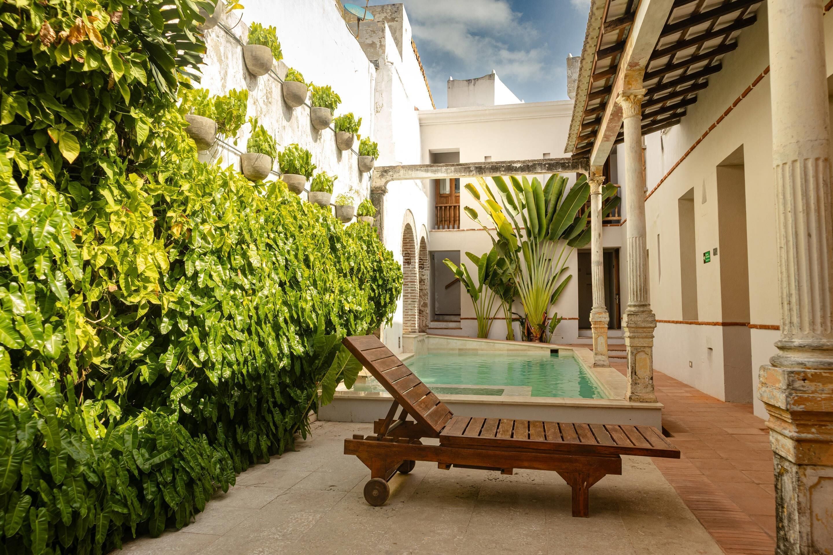 A poolside area with a lounge chair, a wall of greenery, and a pool.