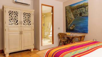 A hotel room with a bed, a wardrobe, a painting, a bathroom, and a small table with chairs.