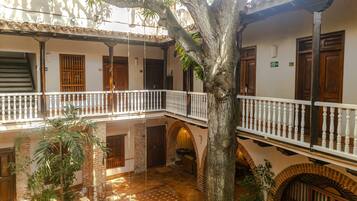 A courtyard with a tree, a staircase, and a balcony with a white balustrade.