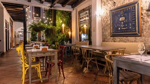 Un comedor interior con mesas y sillas de madera, una pared de piedra con un menú enmarcado y luces colgantes.