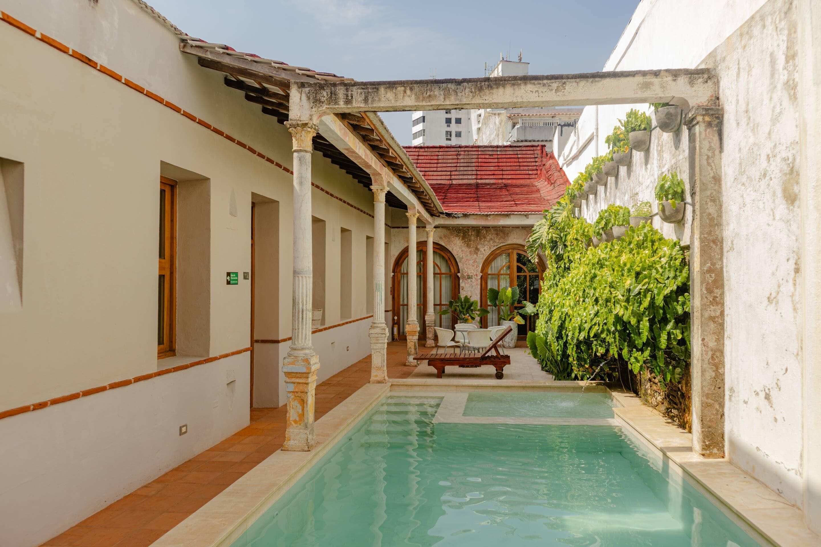 A pool area with a lounge chair, columns, and potted plants.