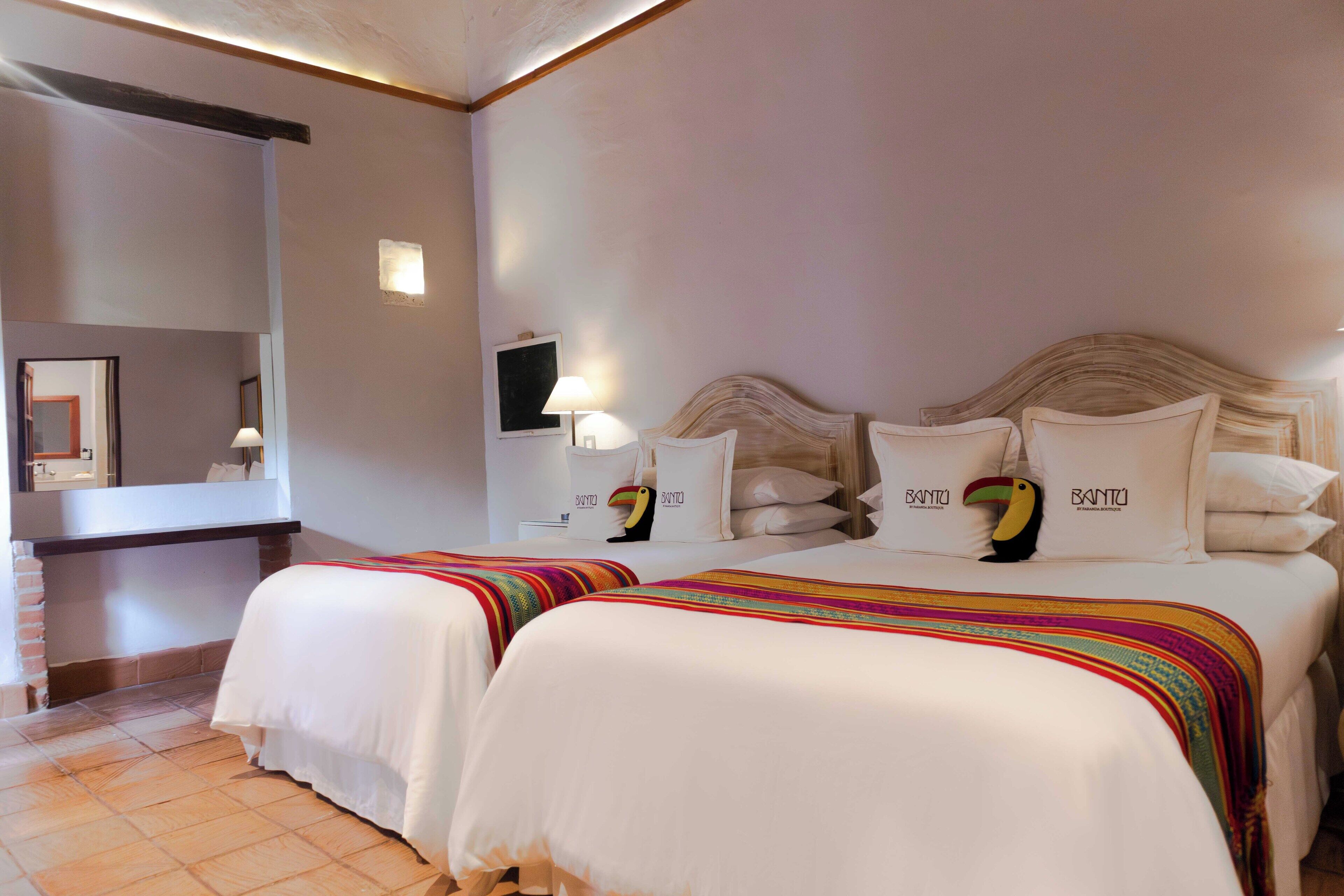 A hotel room with two beds, a large mirror, a flat-screen TV, and a small table with a lamp.