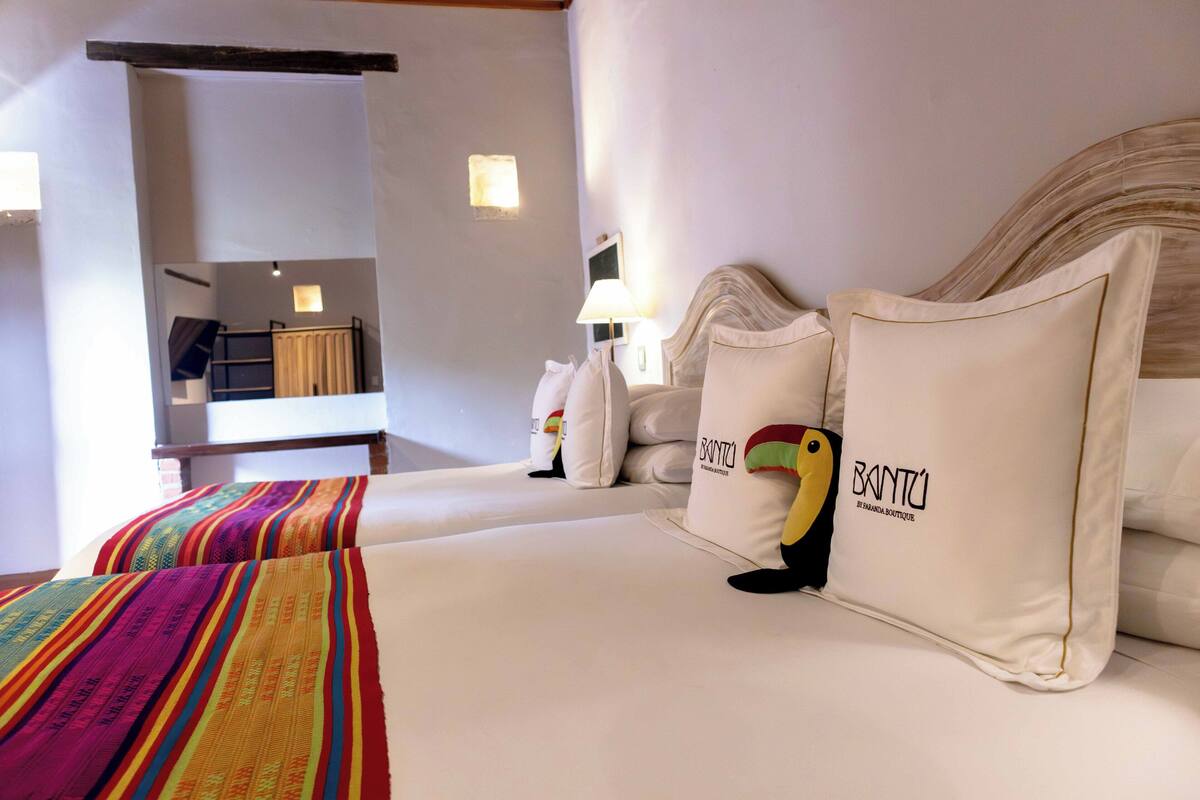 Habitación de hotel con cama, almohadas, lámpara y estante en la pared.