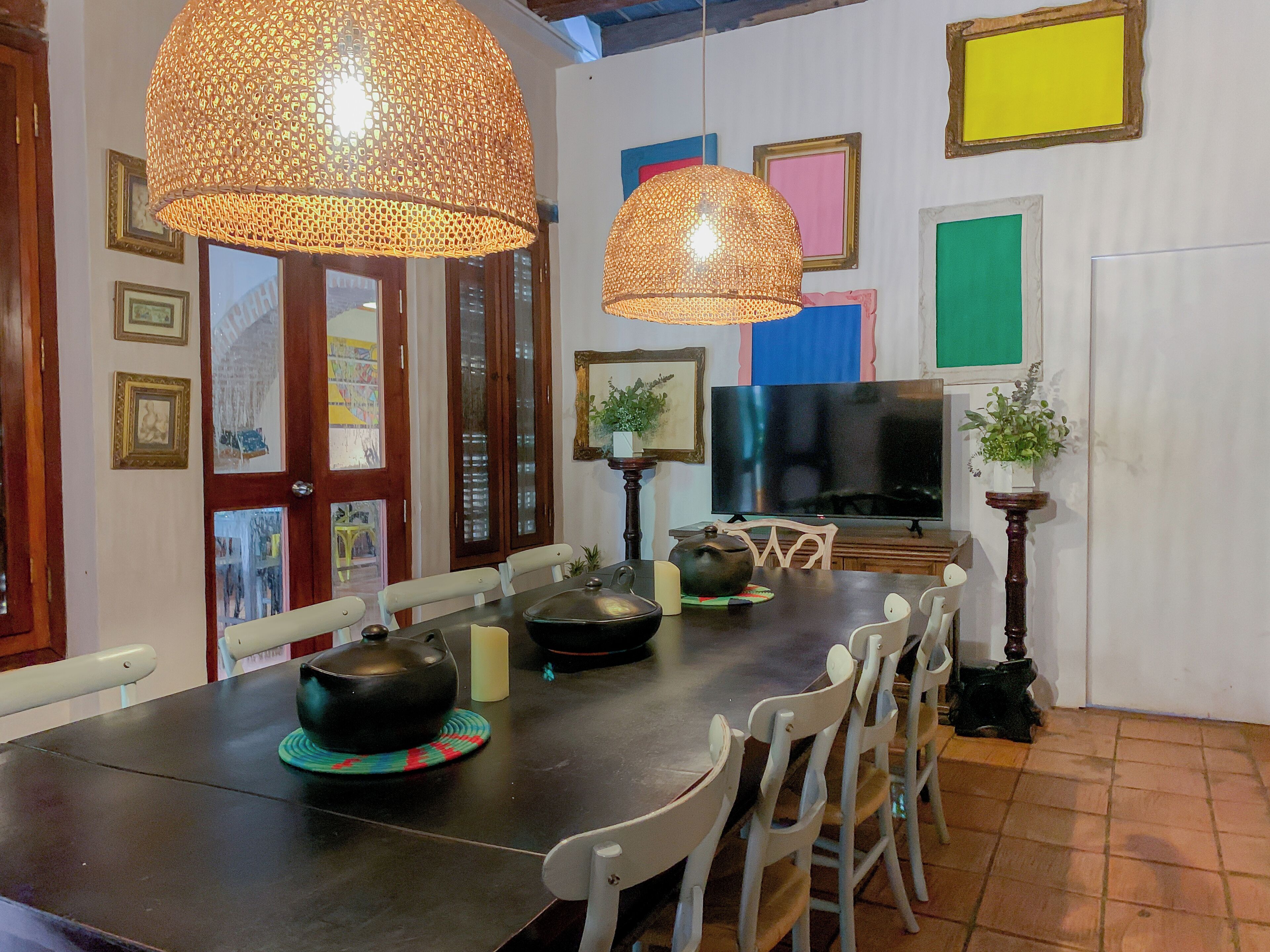 Un comedor con una mesa larga, sillas, un televisor y decoración en la pared.