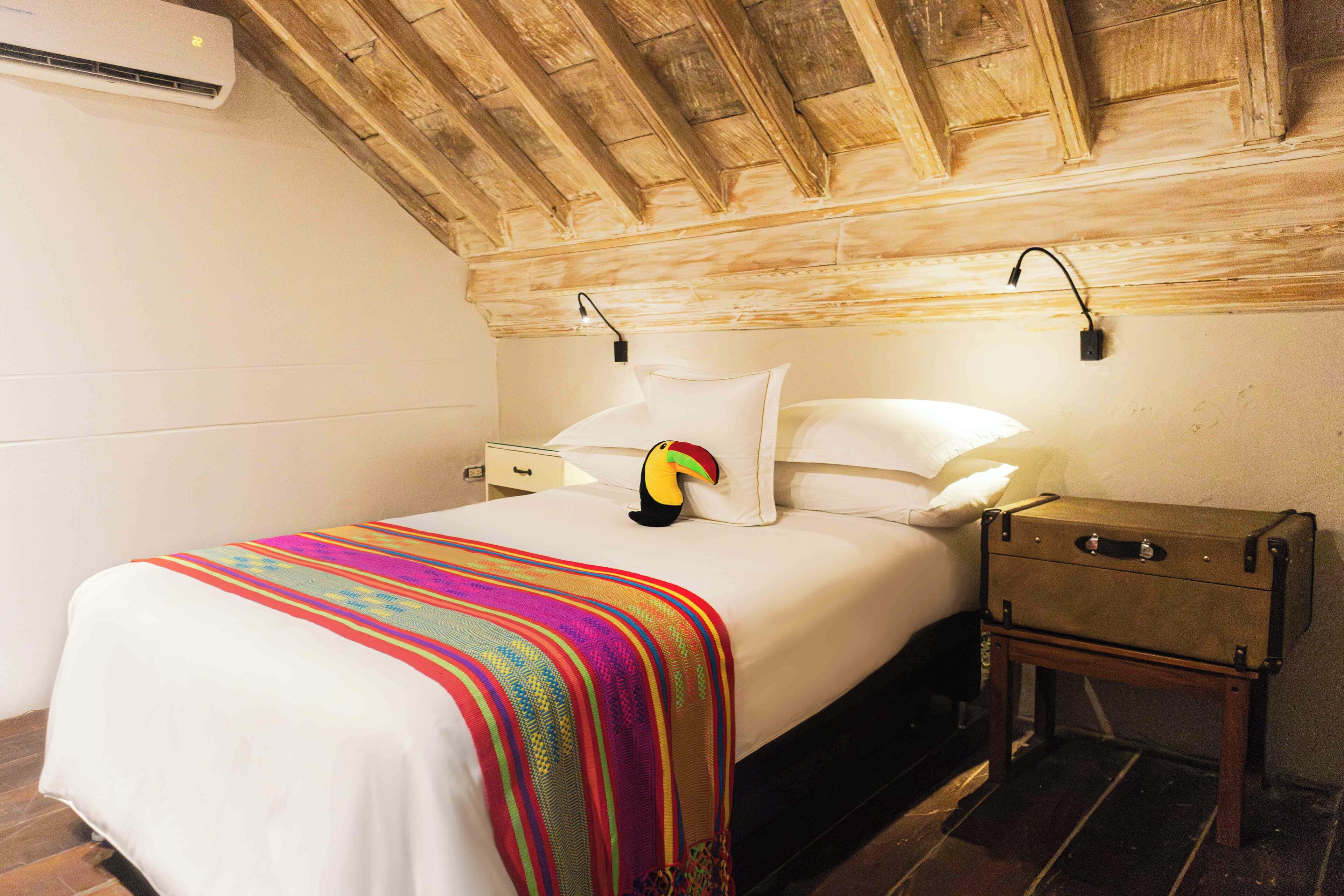 A bedroom with a bed, a colorful blanket, a suitcase, and a nightstand.