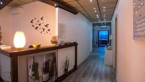 A reception area with a wooden reception desk, a wall-mounted lamp, and a wall art of birds. There is a framed picture on the wall and a potted plant on the floor. - Heraclea Hotel Residence (Policoro)