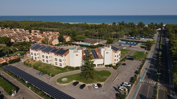 Un hotel con paneles solares en la azotea, piscina y aparcamiento.
