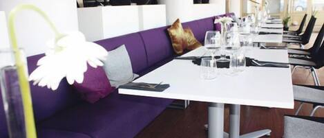 A restaurant with purple seating, white tables, and a modern interior design.