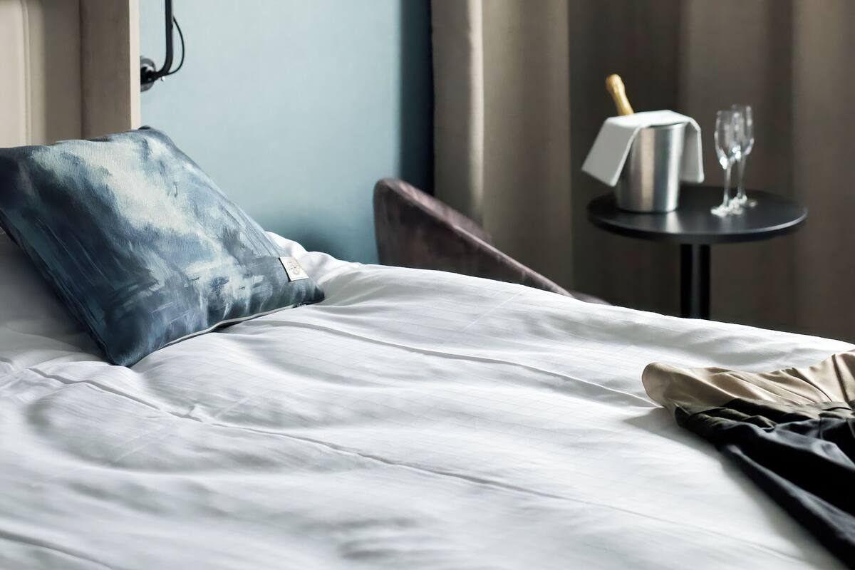 A neatly made bed with white linens, a blue pillow, and a black lamp on a bedside table.