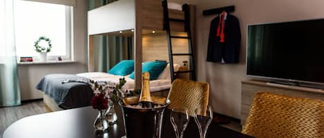 Habitación de hotel con literas, un televisor, una mesa de comedor con una botella de champán y copas, y una ventana con cortinas.