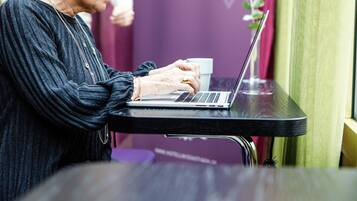 A person using a laptop at a table with a cup and a plant in the background.