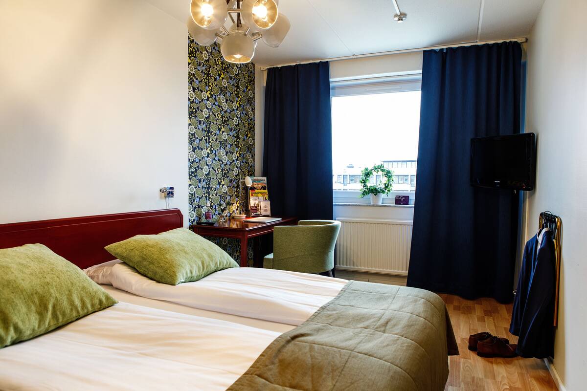 A hotel room with a bed, a desk, a chair, a TV, and a window with curtains.