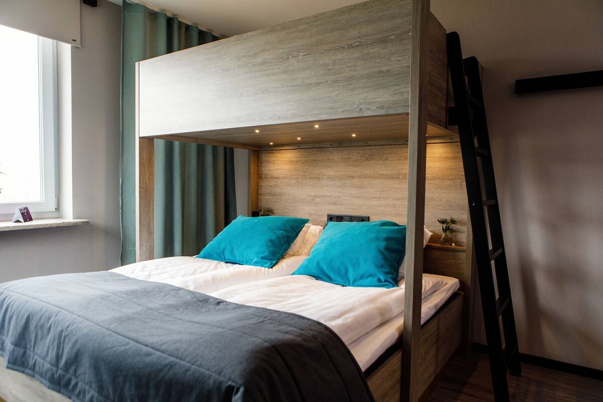 A bunk bed with a wooden headboard, teal pillows, and a black ladder.