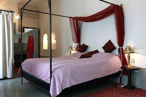 Ein Bett mit Himmelbett, ein Nachttisch mit Lampe und ein roter Teppich mit Muster.