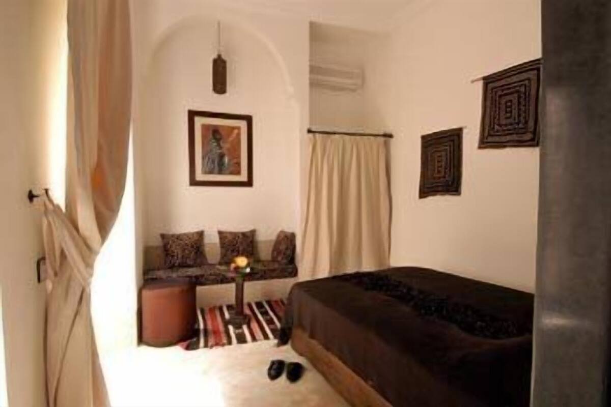 A room with a bed, a sofa, a small table with a lamp, and a picture on the wall.
