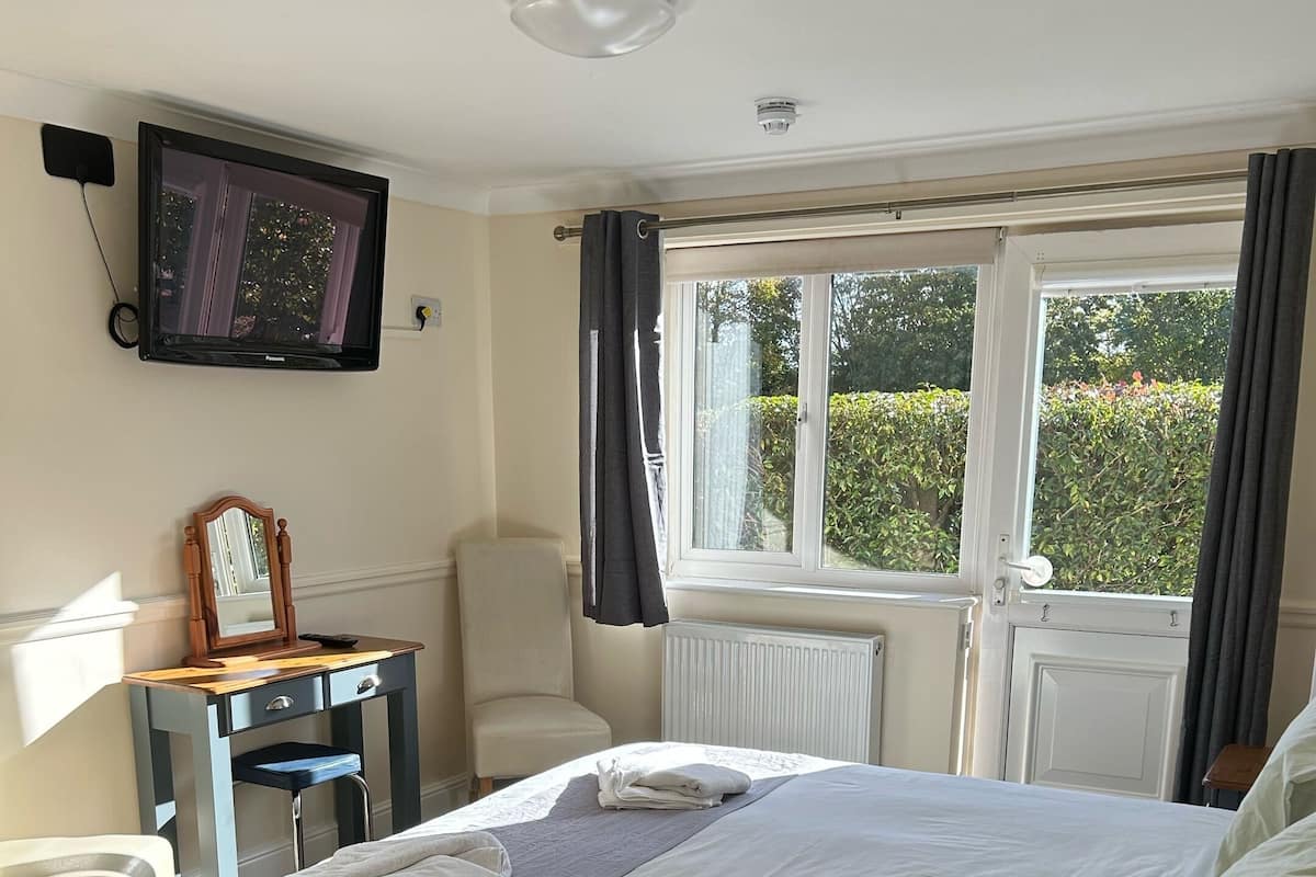 A bedroom with a bed, a desk, a chair, a TV, and a window with curtains.