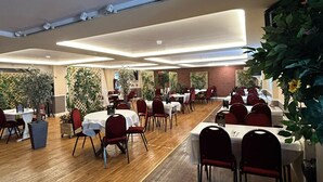 A spacious indoor dining area with multiple tables and chairs, wooden flooring, and potted plants. - Halfway House Inn Country Lodge (Yeovil)