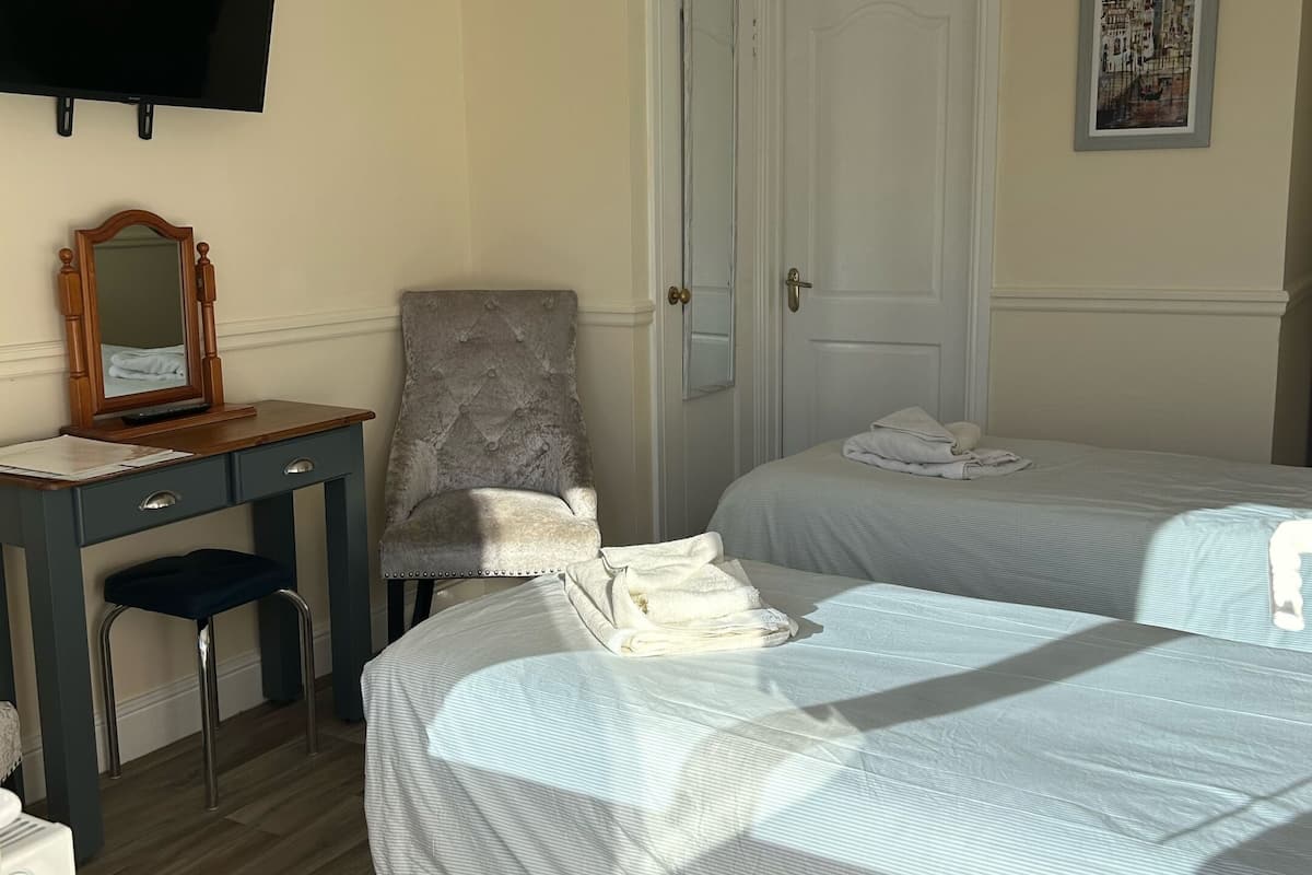 A hotel room with two beds, a desk with a chair, a television, and a door.