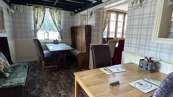 Una habitación con una mesa y sillas de madera, una alfombra estampada y una ventana con cortinas.