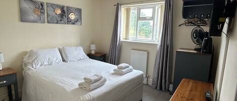 A bedroom with a bed, bedside tables, a desk, a television, and a window with curtains.
