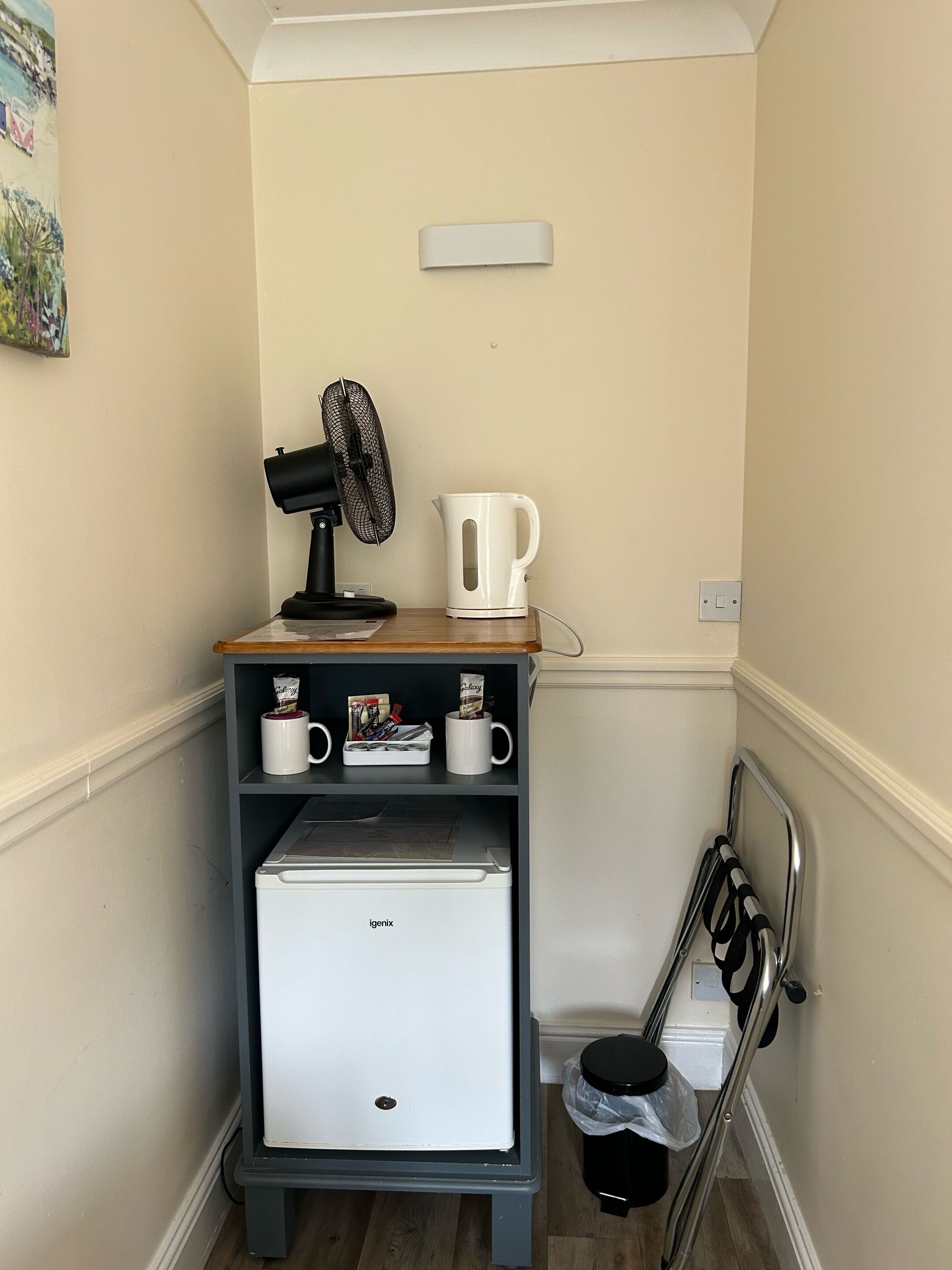 A compact kitchenette with a coffee maker, a fan, and a small refrigerator.