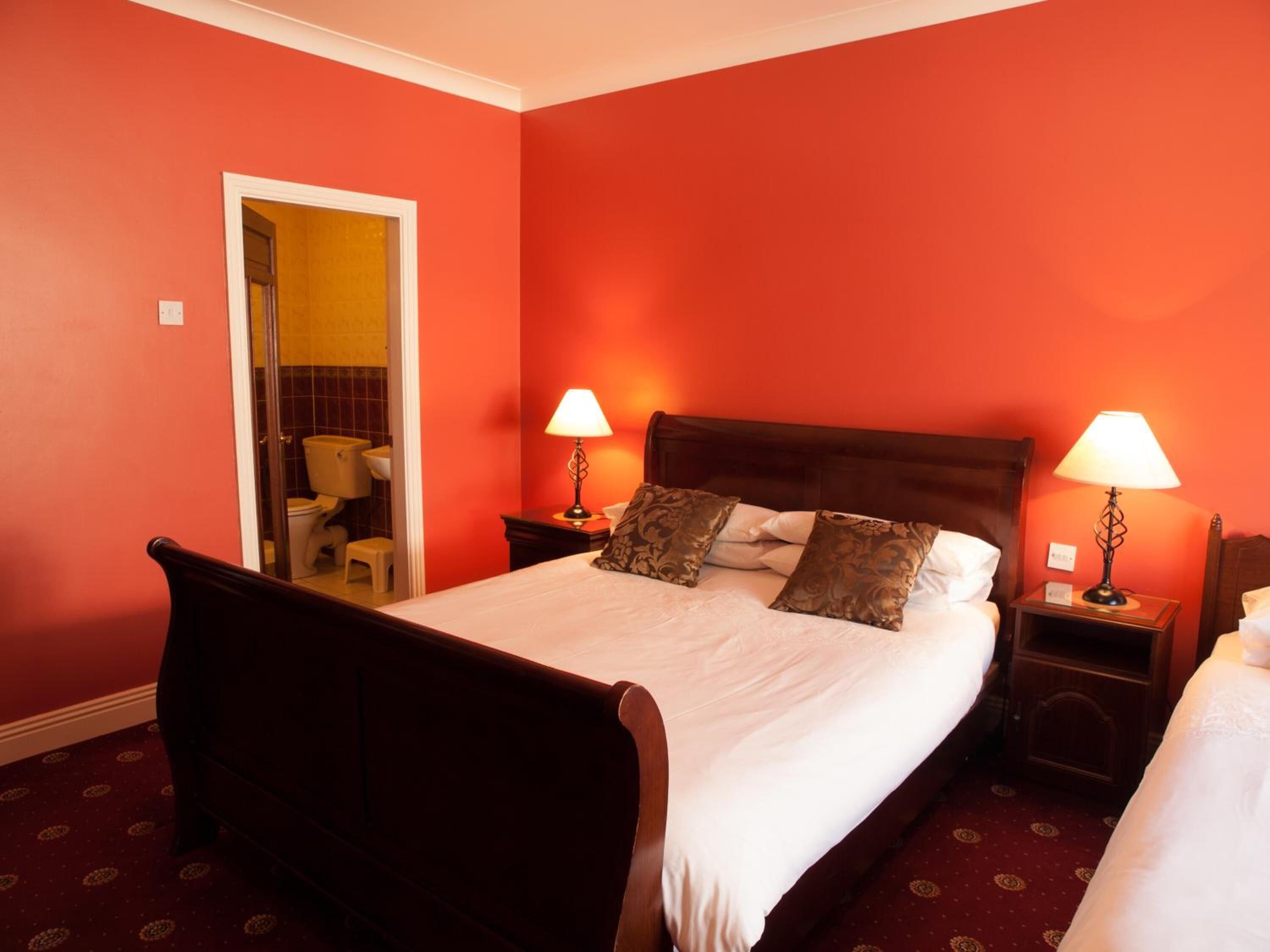 A hotel room with a large bed, two bedside tables with lamps, a wooden headboard, and a view of the bathroom.