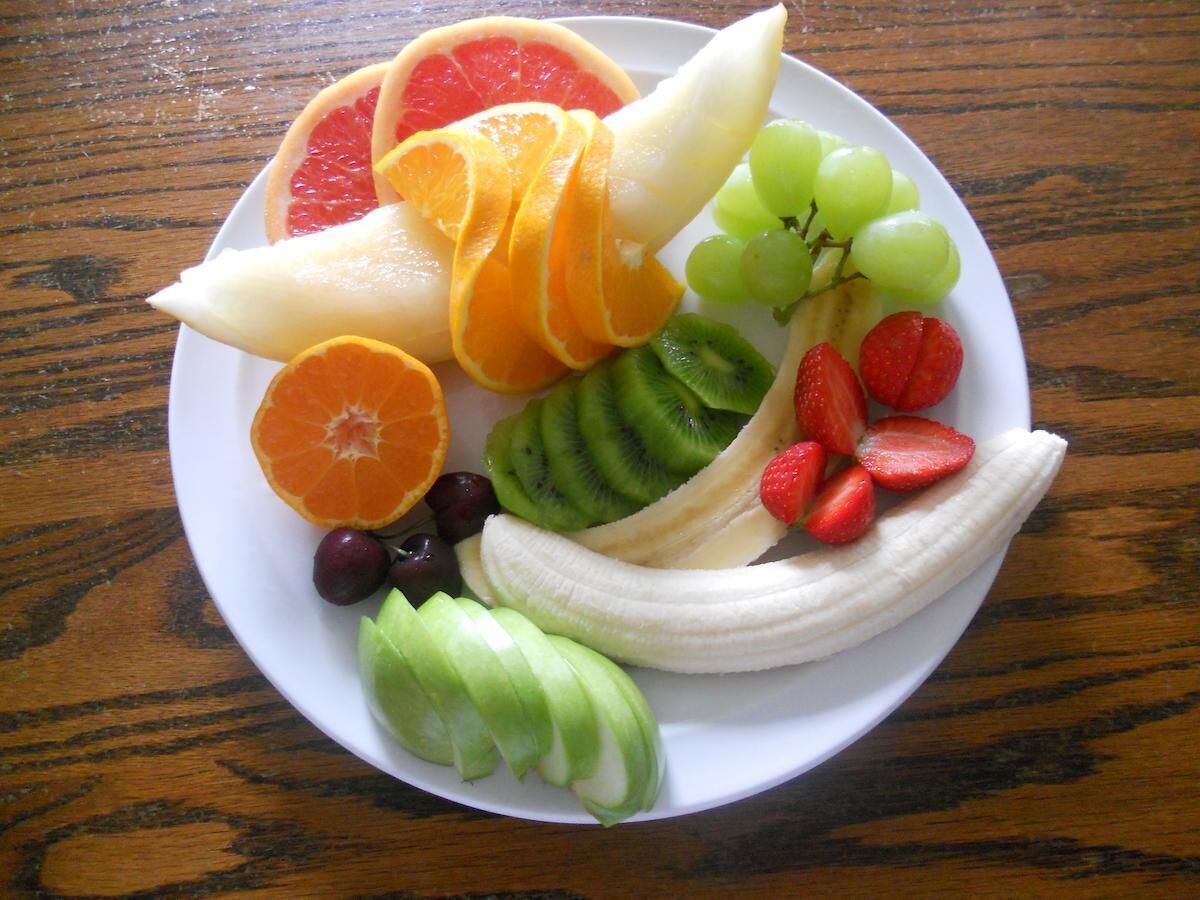 A plate of assorted fruits including grapes, strawberries, kiwi, orange slices, and banana.