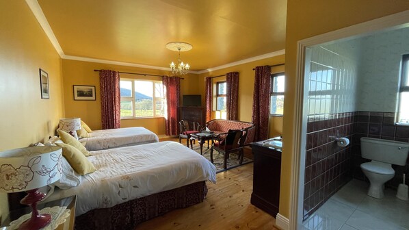 Habitación de hotel con dos camas, una mesa de comedor, un sofá, una araña y un baño con inodoro y lavabo.