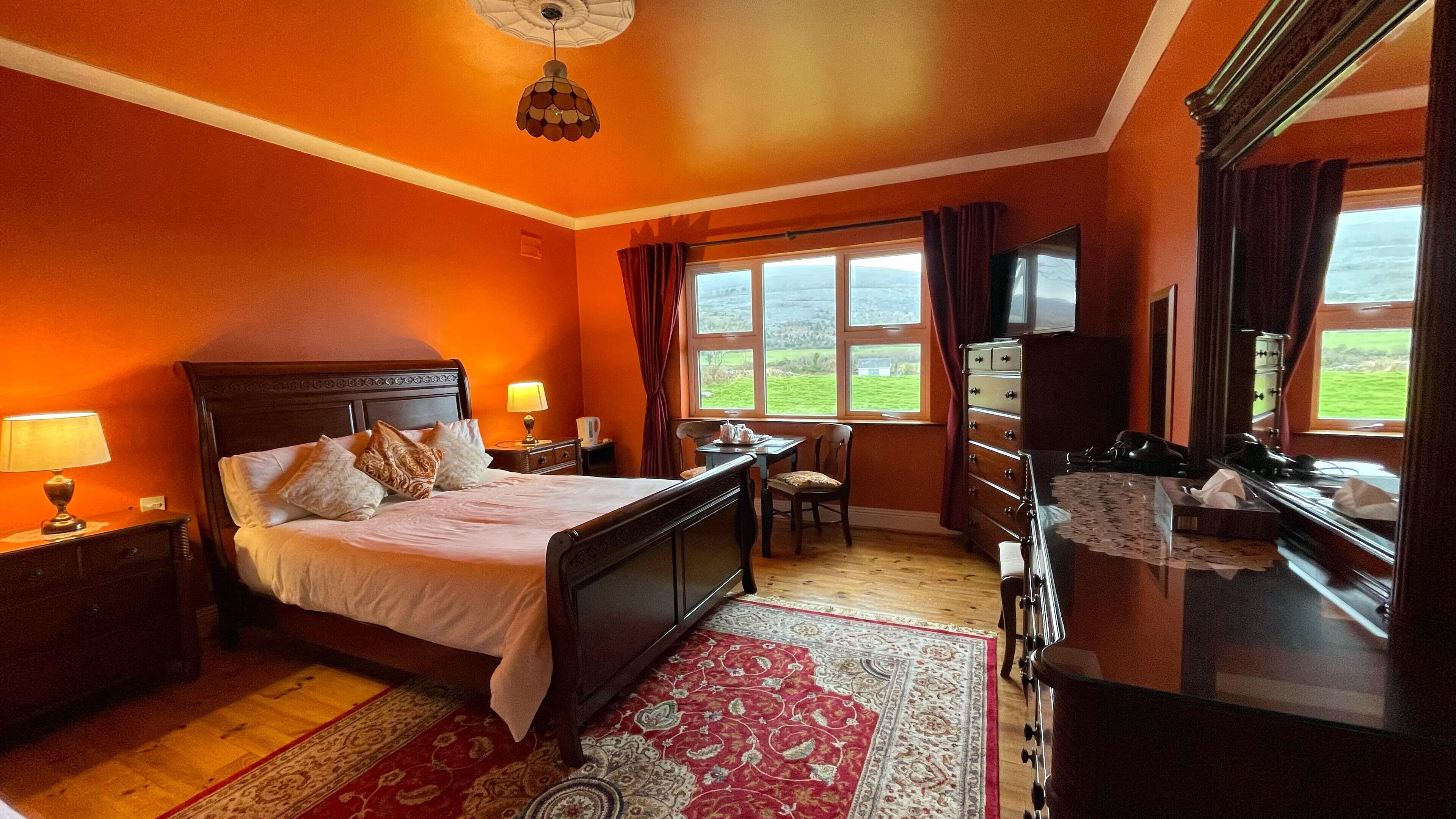 Habitación de hotel con cama, escritorio, cómoda, televisor y ventana con vista al exterior.