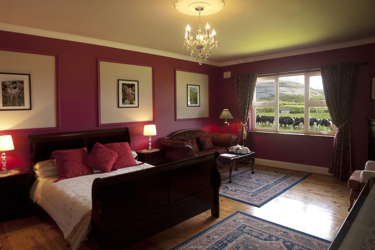 A bedroom with a large bed, two bedside tables with lamps, a chandelier, and framed pictures on the wall.