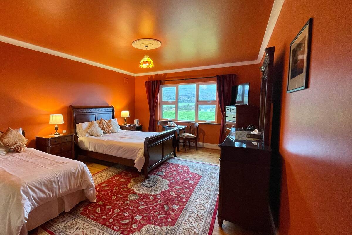 A hotel room with two beds, a desk, a chair, a TV, and a window with a view of the outdoors.