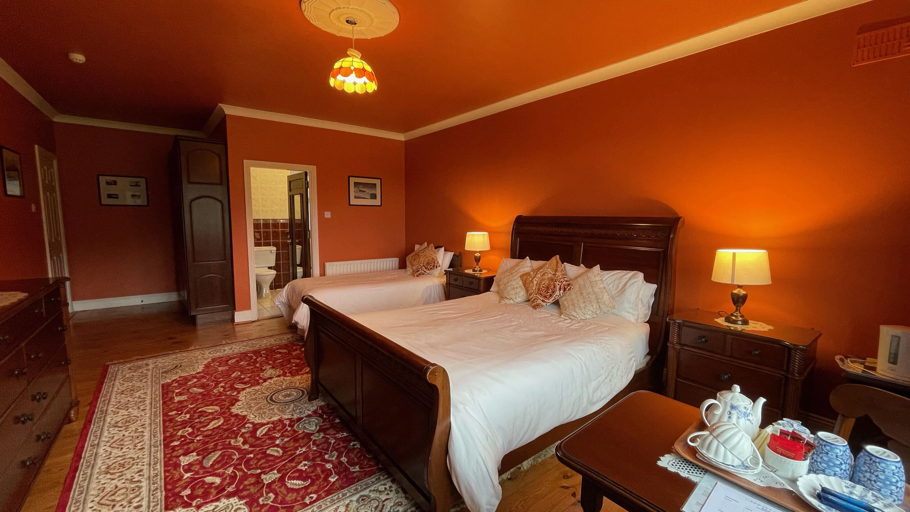 A hotel room with two beds, a red carpet, a wooden dresser, and a nightstand with a lamp.