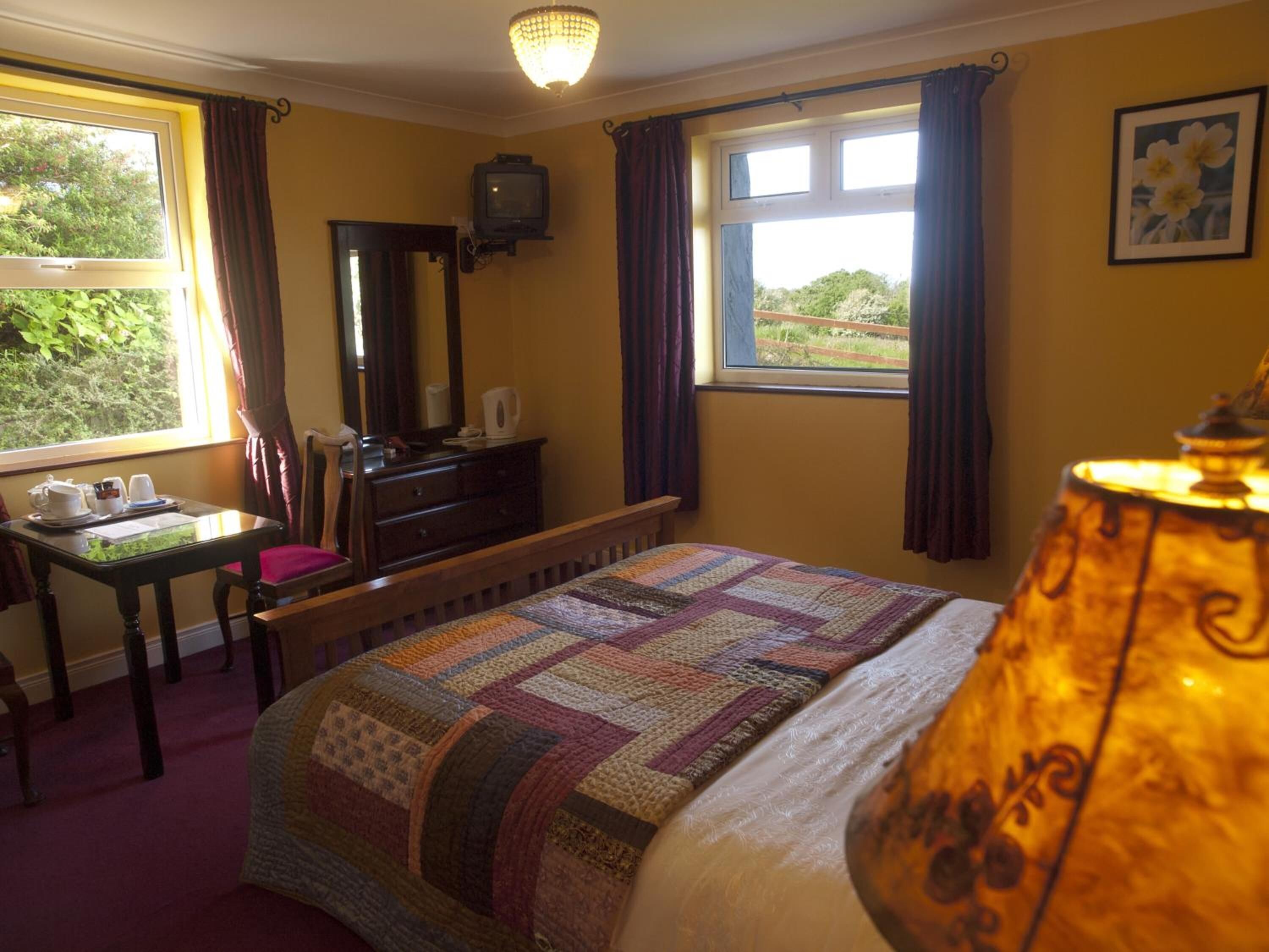 A bedroom with a bed, a desk with a chair, a dresser, a television, and a window with curtains.
