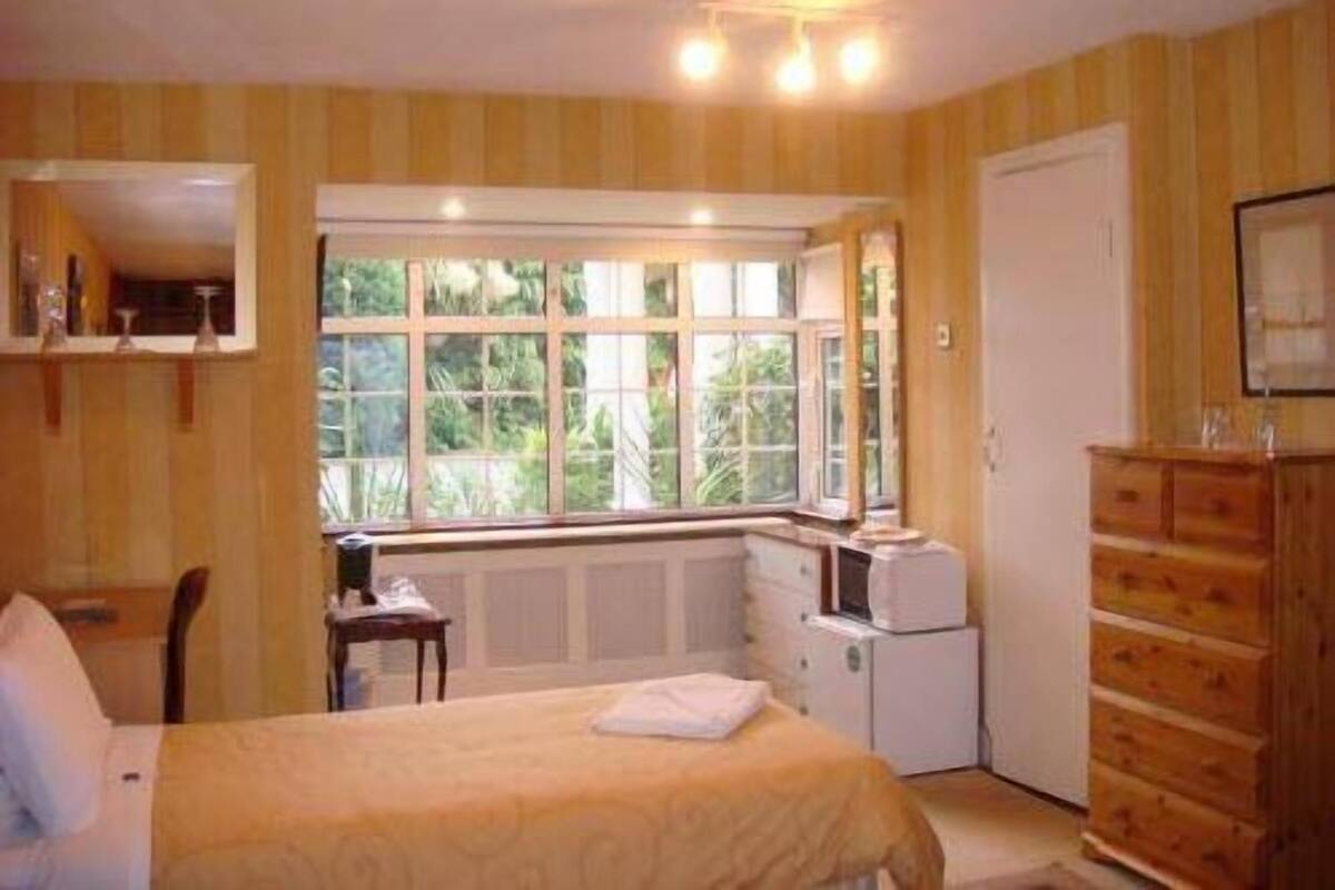 A bedroom with a bed, a dresser, a desk, and a window with a view of greenery.