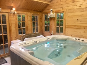 Una cabaña de madera con hidromasaje, ventanas amplias y una lámpara en el techo.