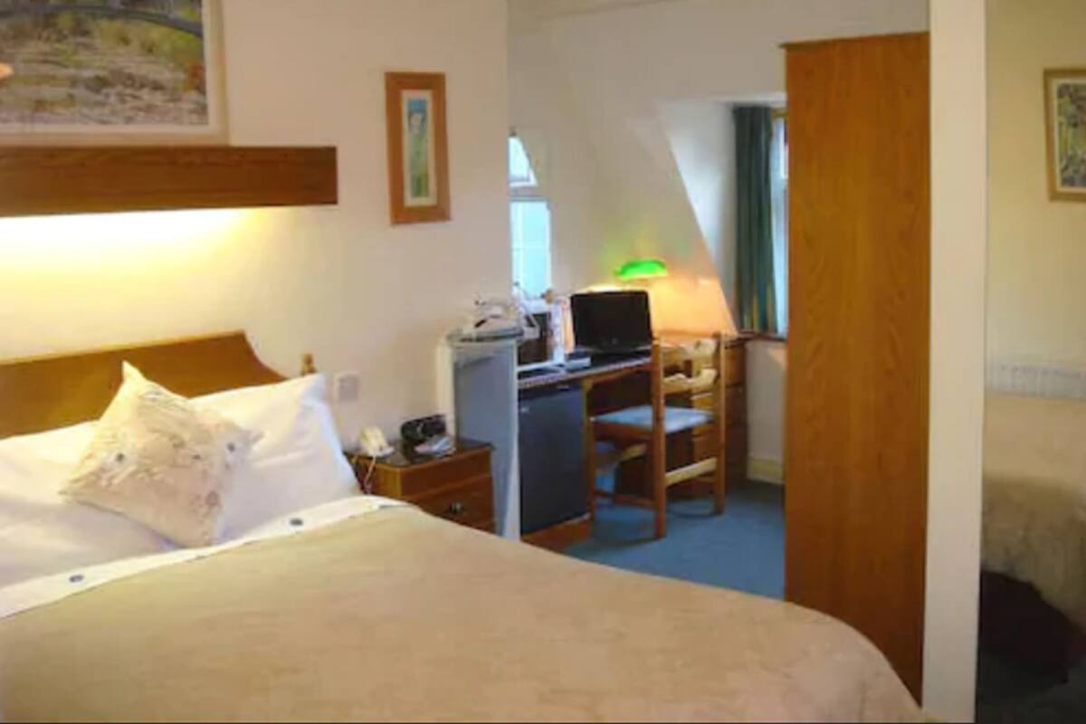 A hotel room with a bed, a desk with a laptop, a chair, and a lamp.