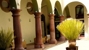 Un patio con una fuente de agua, plantas en macetas y un edificio con arcos y columnas.