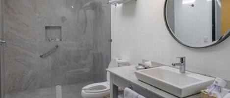 Un baño moderno con ducha de mármol, inodoro, lavabo y espejo.