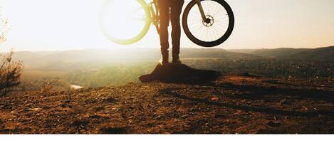 Una persona sobre terreno rocoso sosteniendo una bicicleta, con un extenso paisaje al fondo.