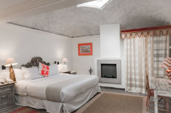 Un dormitorio con cama, mesitas de noche, chimenea y ventana con cortinas.