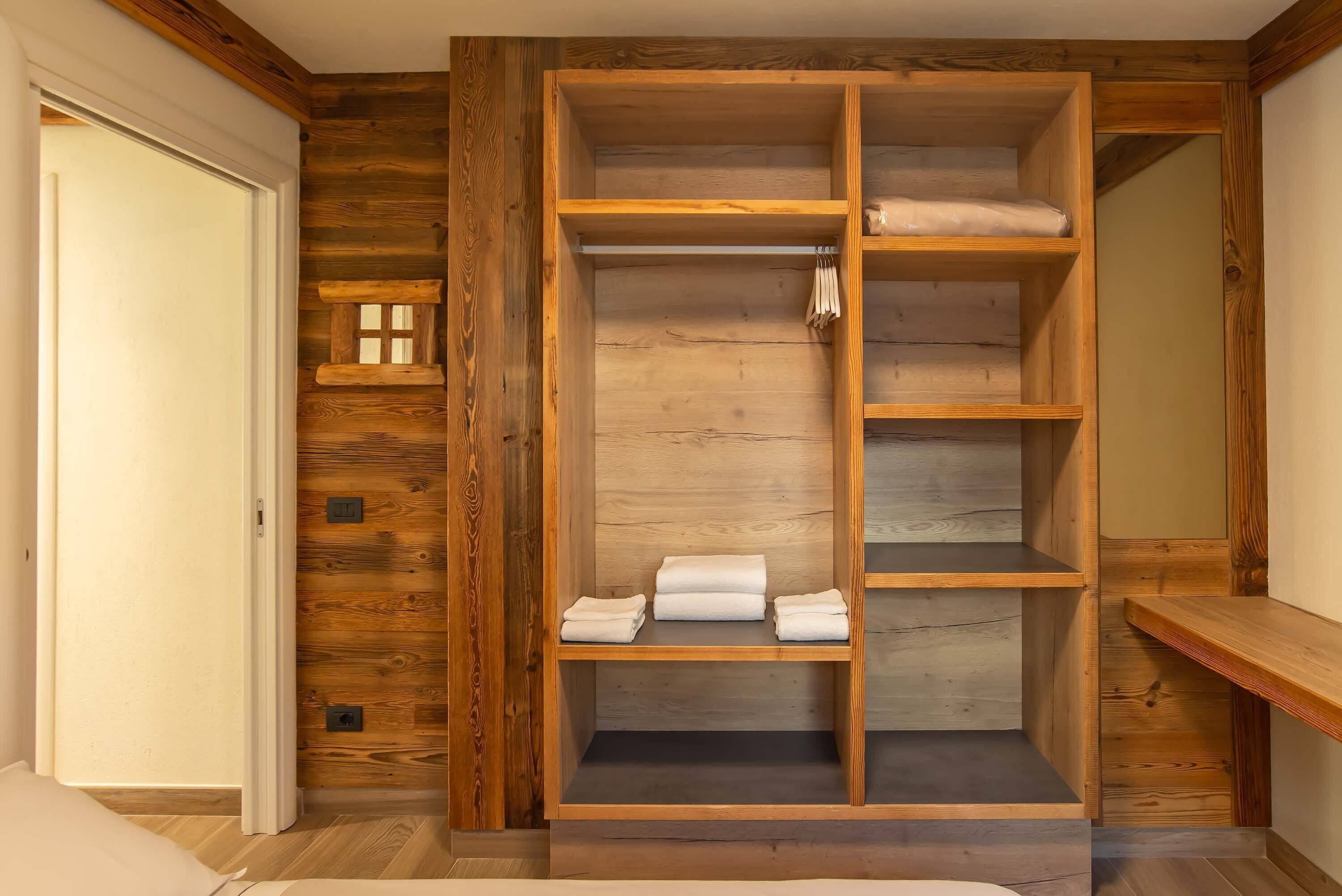 Un armario empotrado de madera con varios estantes y espacio para colgar, situado en una habitación con paneles de madera.