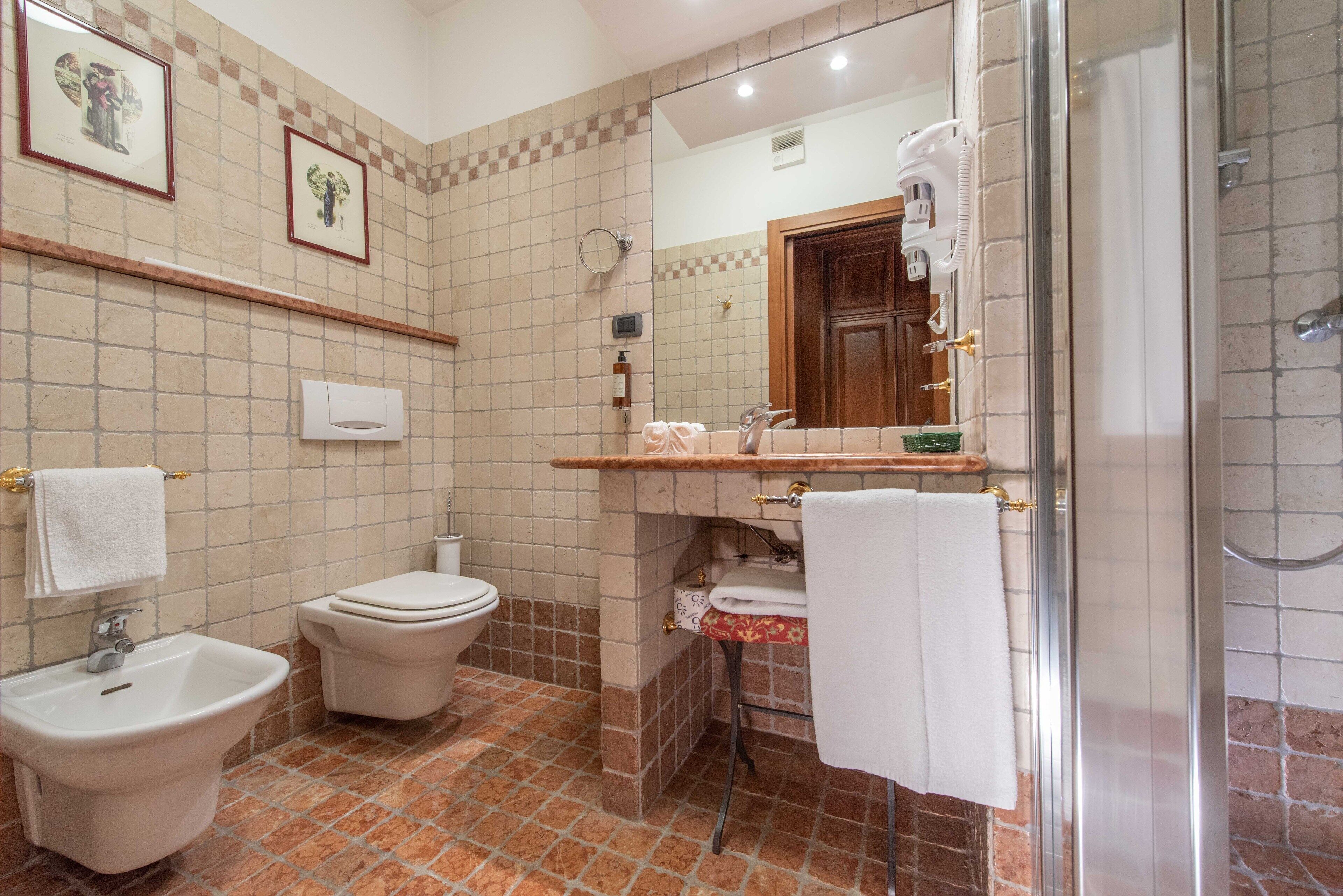 A bathroom with a bidet, toilet, sink, and a glass-enclosed shower.
