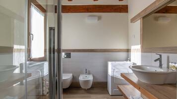 A modern bathroom with a glass shower enclosure, a bidet, a sink, and a wooden vanity.