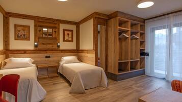 A room with two beds, wooden headboards, a wooden wardrobe, a red chair, and a table.