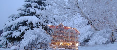Un hotel de varios pisos, árboles cubiertos de nieve y un exterior bien iluminado.